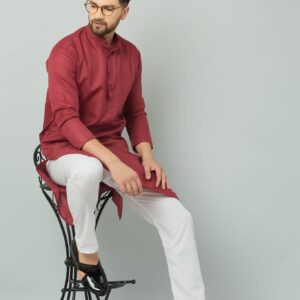 Man in maroon kurta sitting on stool.