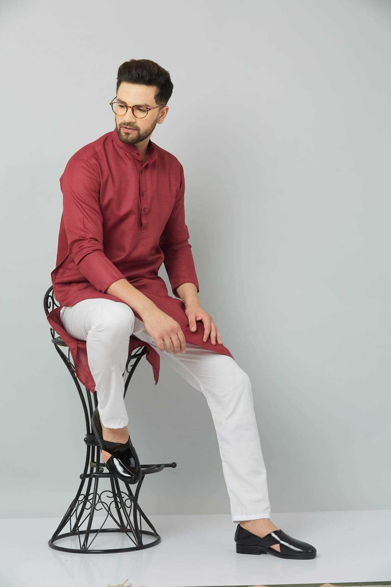 Man in maroon kurta sitting on stool.